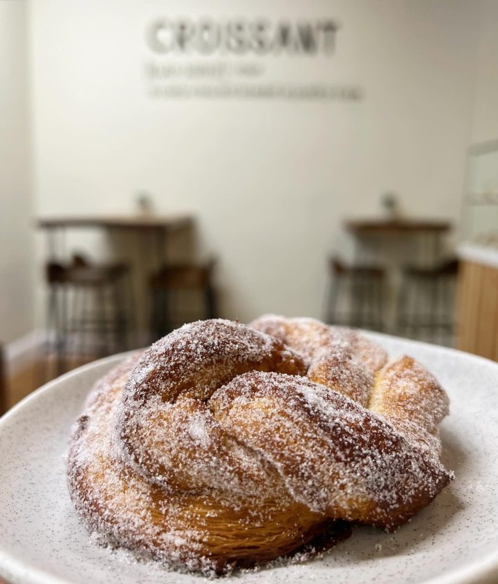 A sugared cinnamon knot on a plate, the caf&eacute; tables behind