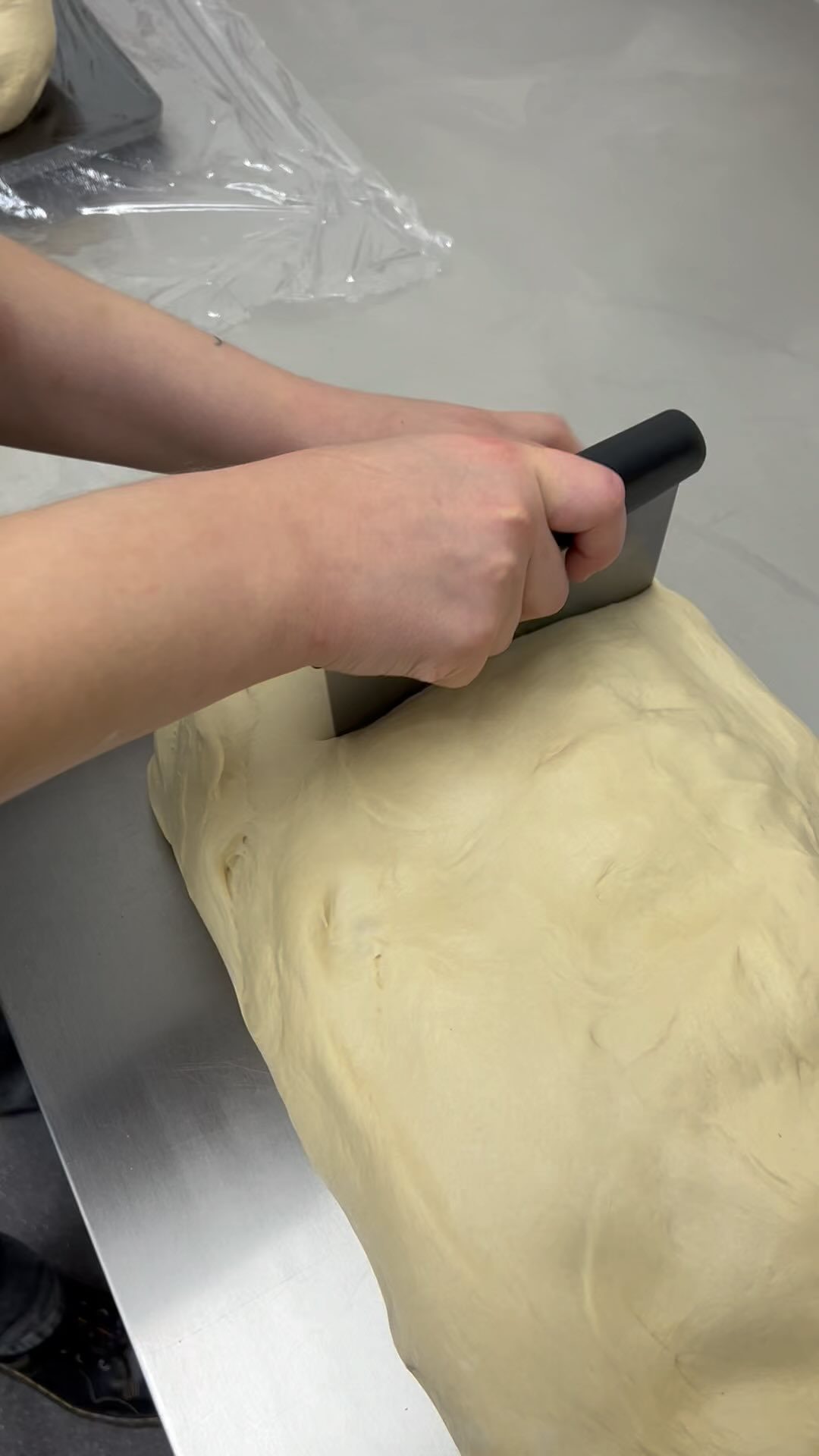 A slab of laminated dough being portioned by hand with a bench scraper