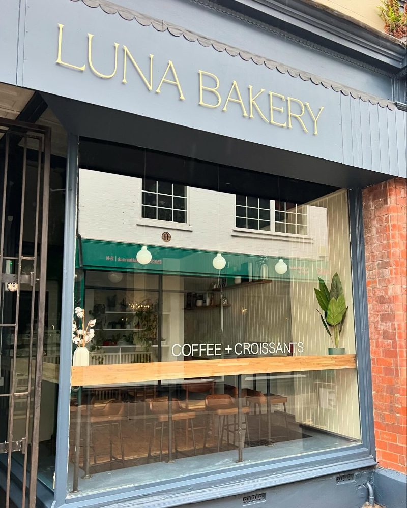 Our shopfront: sage-green fascia, 'coffee + croissants' painted in the window